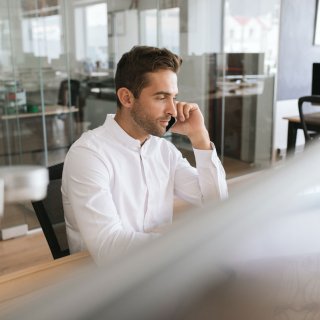 Mann sitzt in Großraumbüro vor seinem Rechner und telefoniert